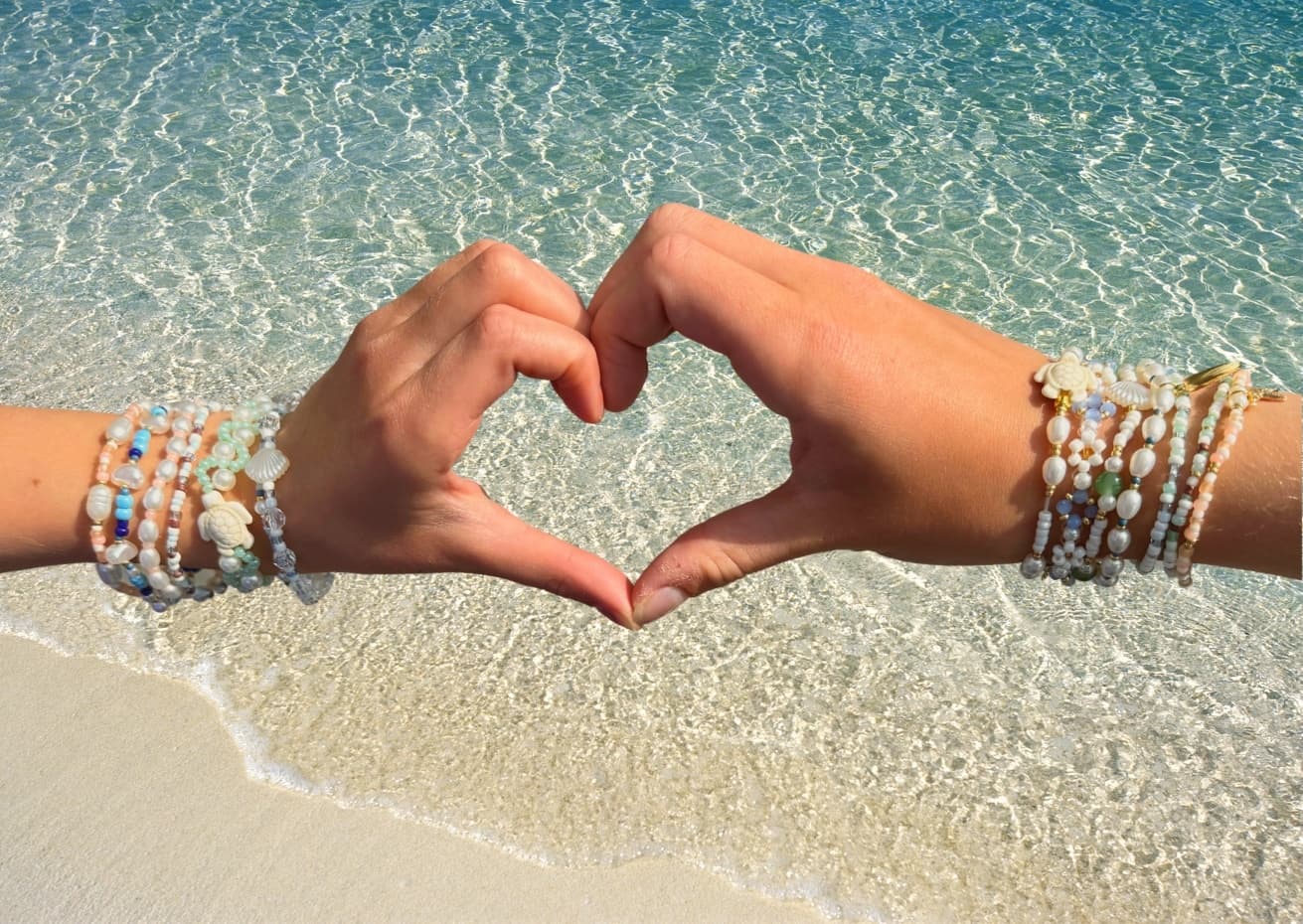 Hands wearing colorful beaded bracelets on beach sand with ocean waves